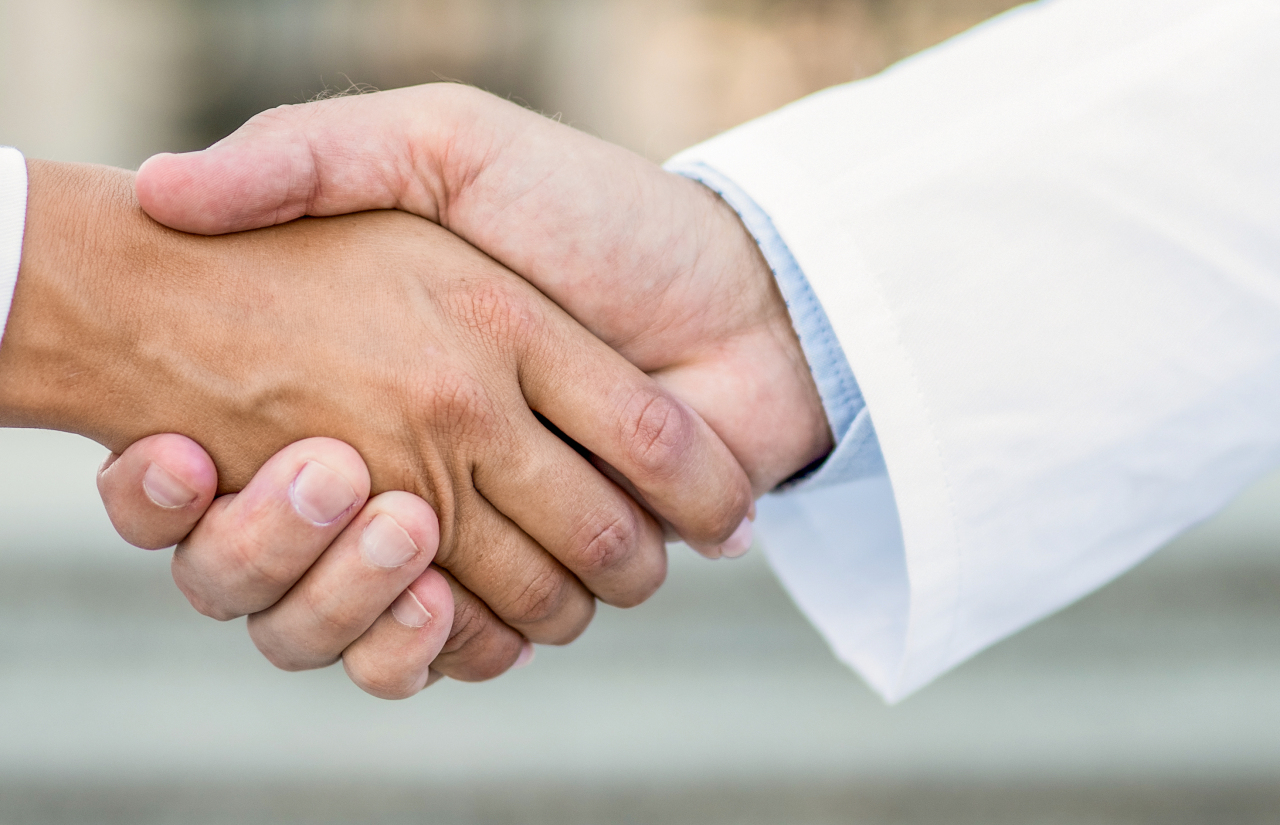 Hand close up of doctors shaking hands outdoors in front of hospital. - Doctors shaking hands. - 1255266318